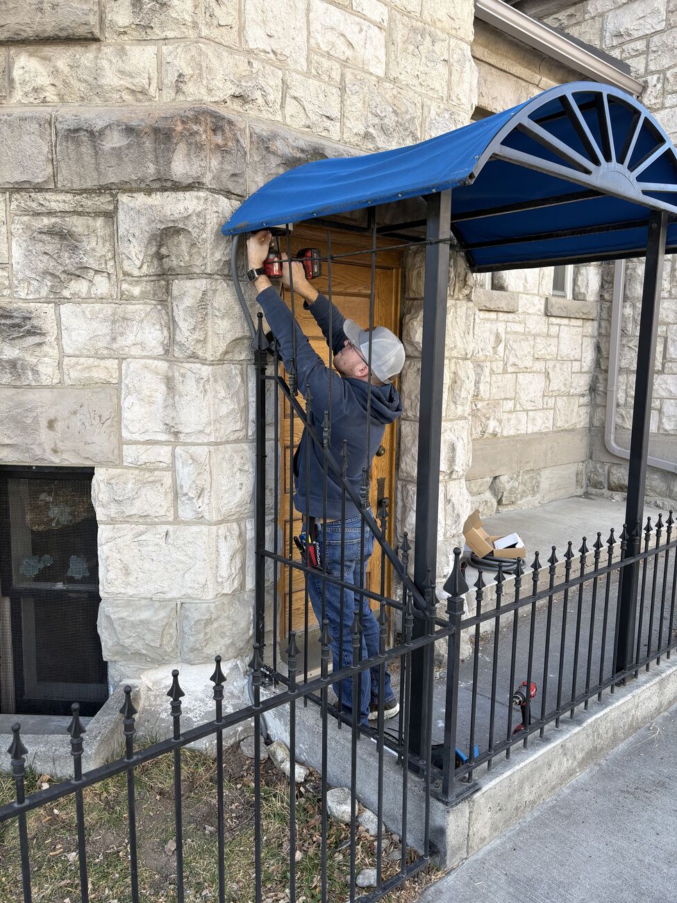A Pine Cove technician installing a security camera on the stone entrance of a client building